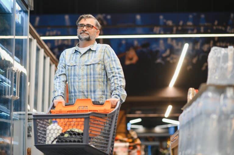Man with shopping cart in a large supermarket aisle